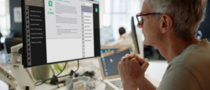 An older man attentively observes an AI chatbot on his screen, reflecting on the intersection of leadership development and artificial intelligence.